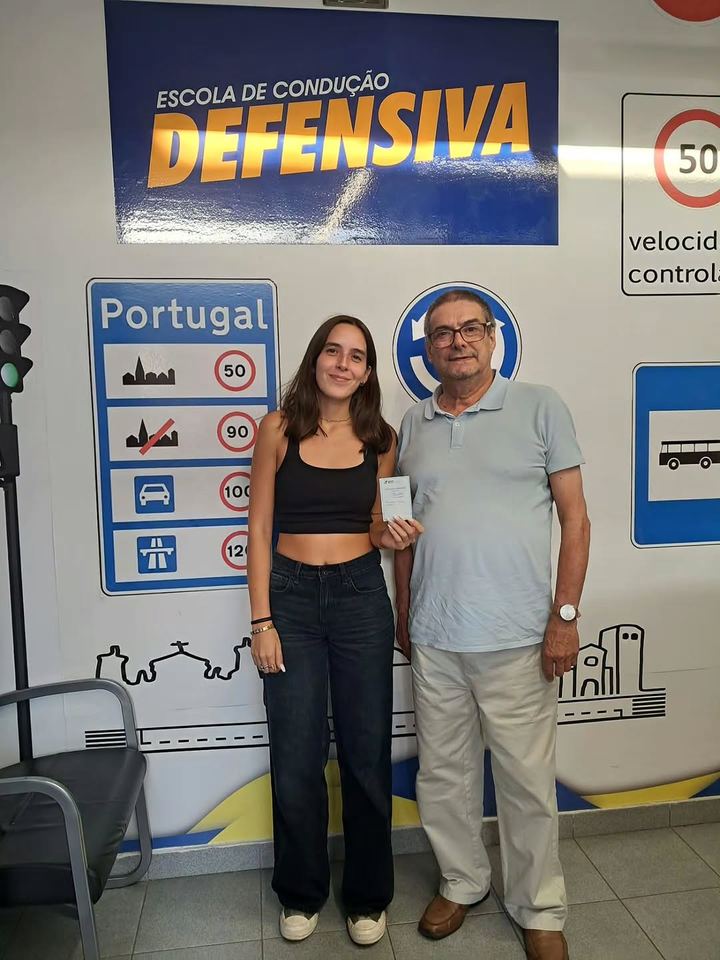 Nova condutora acompanhada, a mostrar a carta em frente à parede de sinais da escola